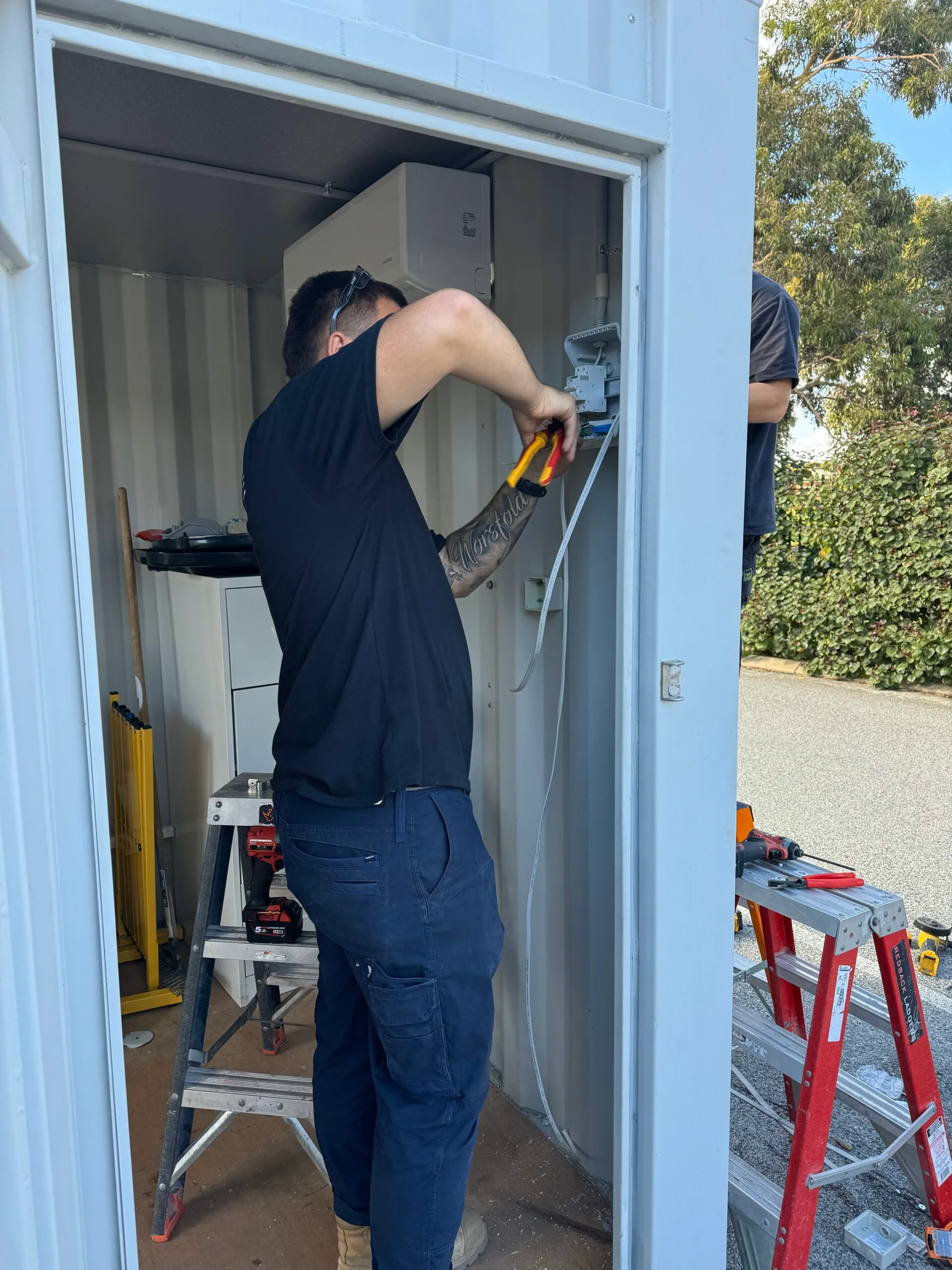 pure electrical and air staff member trimming wires in a shed